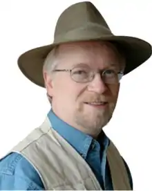 A headshot of Shawn Carlson smiling while wearing a hat