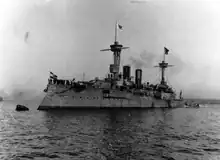 A large warship moored to a buoy, with a group of sailors crowded together on the bow